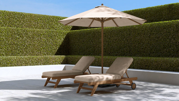 Chic Teak teak sun loungers with wheels and cushions beside a round teak coffee table under a large parasol on a paved terrace.